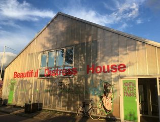 Gebouw van Beautiful Distress met rode letters op de gevel, graffiti op de muur en een fiets bij de ingang.