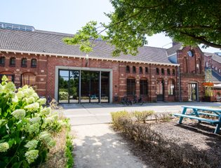 Zuiveringshal Oost in Cultuurdorp Westergas in Amsterdam, een bakstenen gebouw met bomen en planten ervoor. Foto: Cultuurdorp Westergas