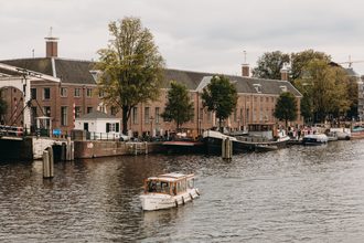 Gebouw van het H'ART Museum aan de Amstel, vroeger de Hermitage Amsterdam, gezien vanaf de Blauwbrug, met boten op het water.
