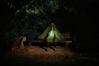 Persoon op bankje met een poncho over het hoofd