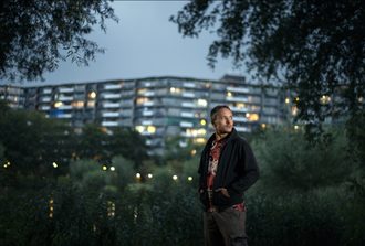 Persoon staat in een groene omgeving met op de achtergrond een flat