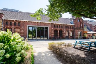 Zuiveringshal Oost in Cultuurdorp Westergas in Amsterdam, een bakstenen gebouw met bomen en planten ervoor. Foto: Cultuurdorp Westergas