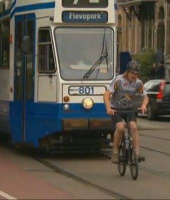 Fietser rijdt over de trambaan voor een blauwe tram van lijn 7 richting Flevopark