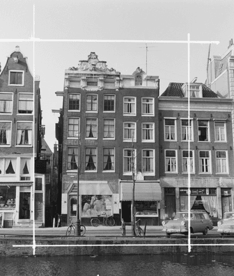 Zwart-witfoto van huizen aan een Amsterdamse gracht met geparkeerde auto's en fietsen.