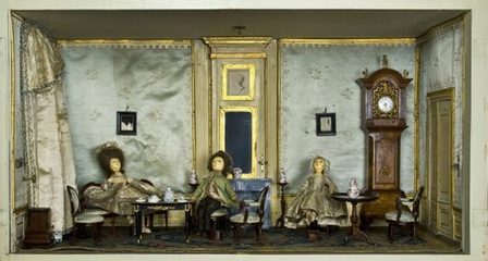 De salon van het ‘Grote poppenhuis’, met de geborduurde zijden wandbespanning, de bijpassend beklede stoelen, de rijke zijden gordijnen, de tot in detail aangeklede poppen en het geborduurde vloerkleed.