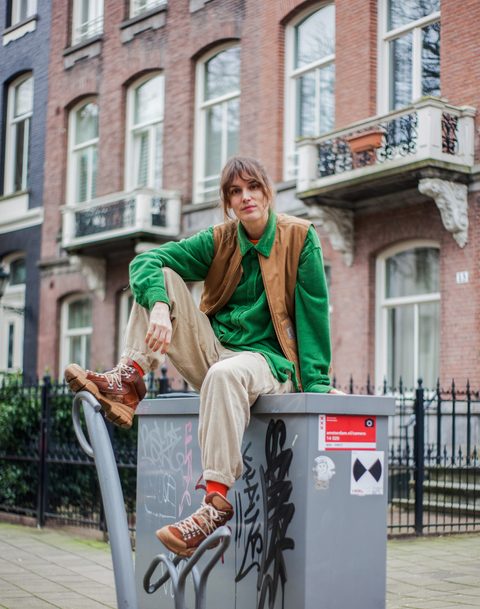 Lize Korpershoek zit op een elektriciteitskast. Achter haar staan huizen, waaronder het huis waarin Aletta Jacobs heeft gewoond. Lize Korpershoek sitting on an electricity box. Behind her are houses, including the house in which Aletta Jacobs lived.