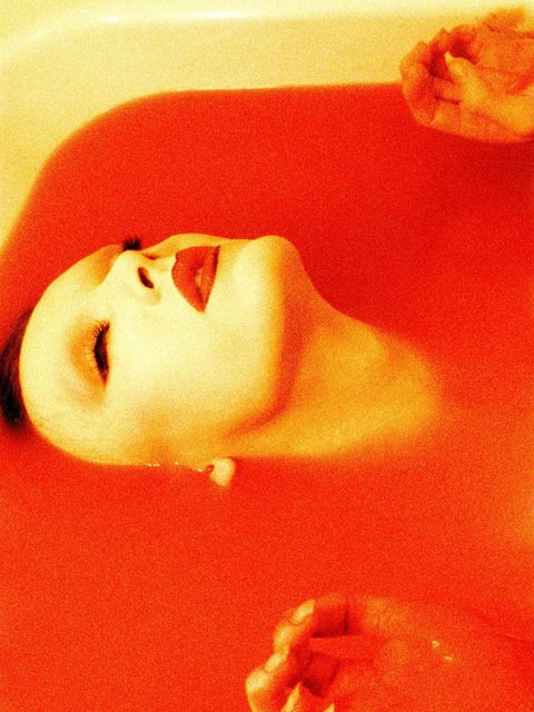 Persoon met rode lippenstift in bad met rood water