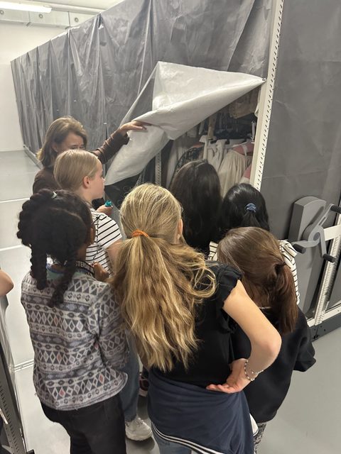 Groep kinderen kijken in depot naar modestukken .