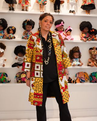 Portret van Ellen Brudet voor een wand met poppen.
Portrait of Ellen Brudet in front of a wall with dolls.
