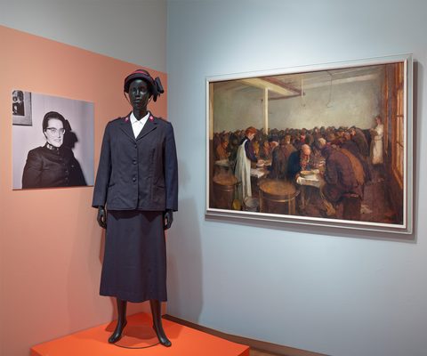 Pop met het kostuum van Majoor Boshardt aan en een schilderij op de muur.
