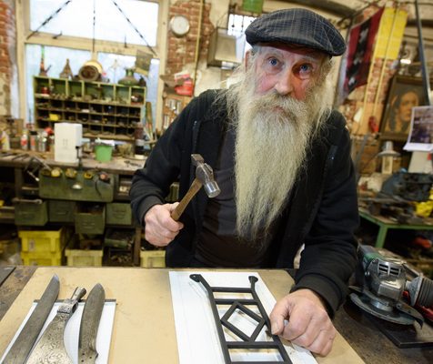 Portret van Bert Meister aan het werk met een hamer en een kunstwerk in zijn handen,